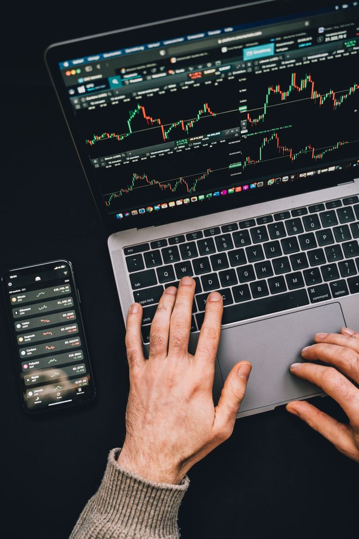 Hands at work on a laptop with cryptocurrency charts and a smartphone screen visible, centered on digital finance.